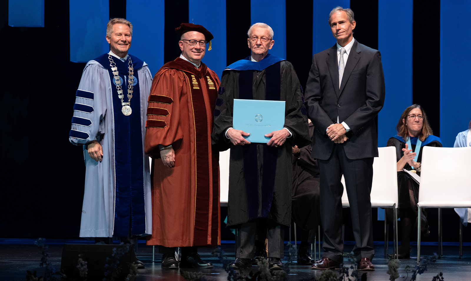 An award winner posing for photos on a stage with University leaders.
