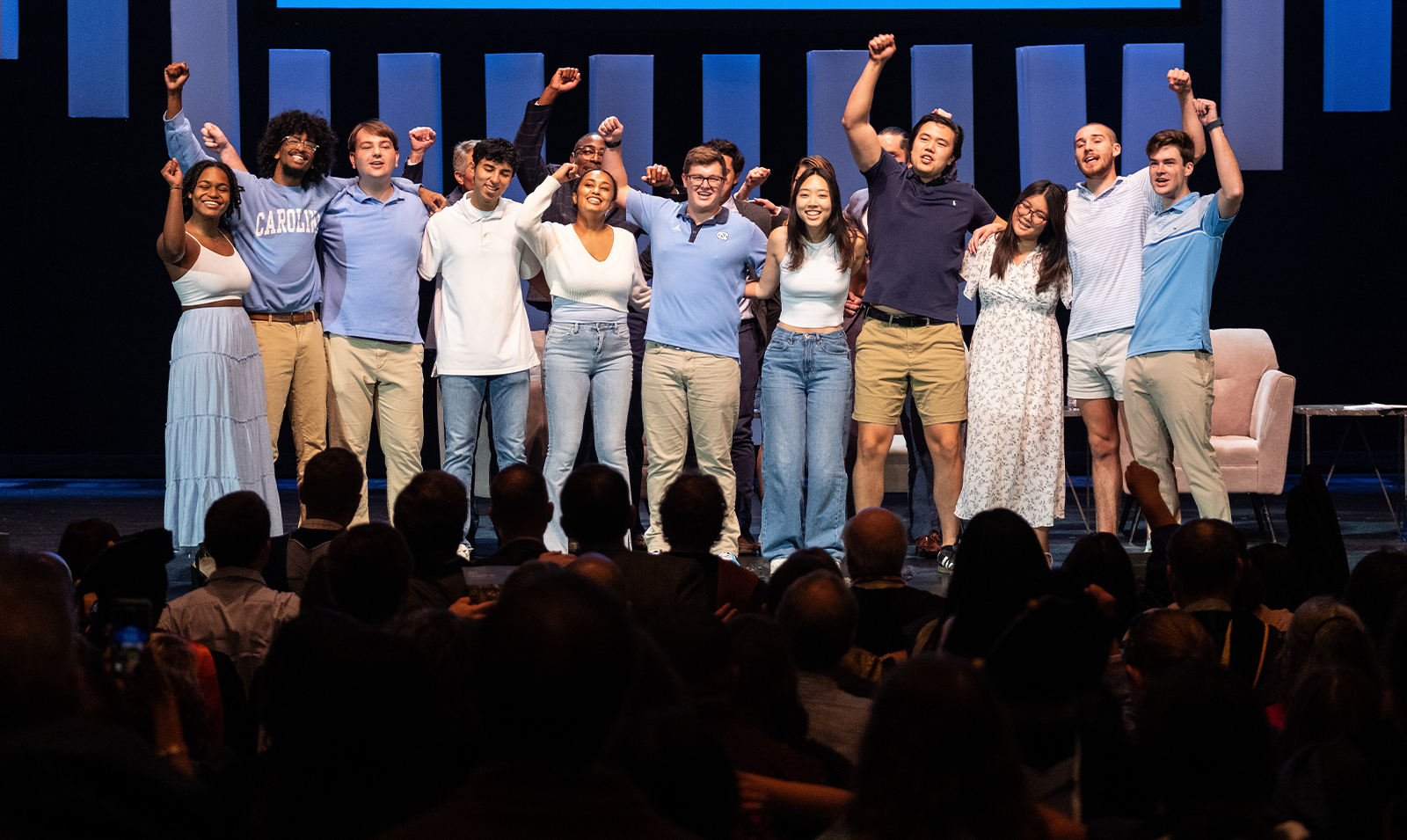 A group of students close together on stage and singing and chanting together.