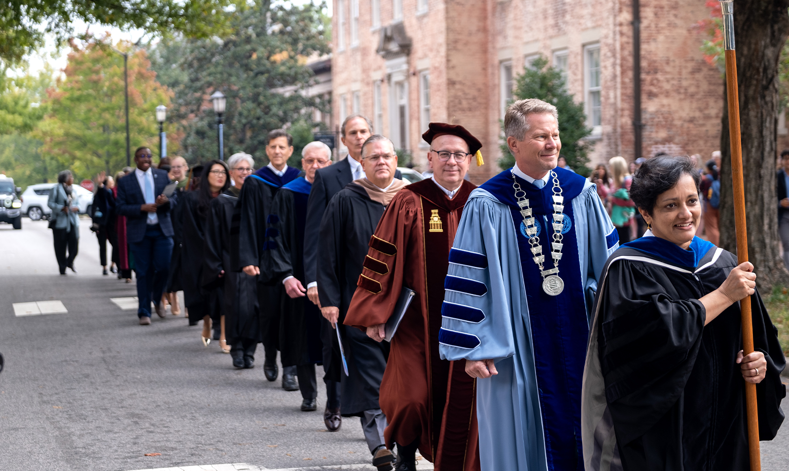A parade of University leaders in regalia walking down a street, Cameron Avenue, during a University Day event.
