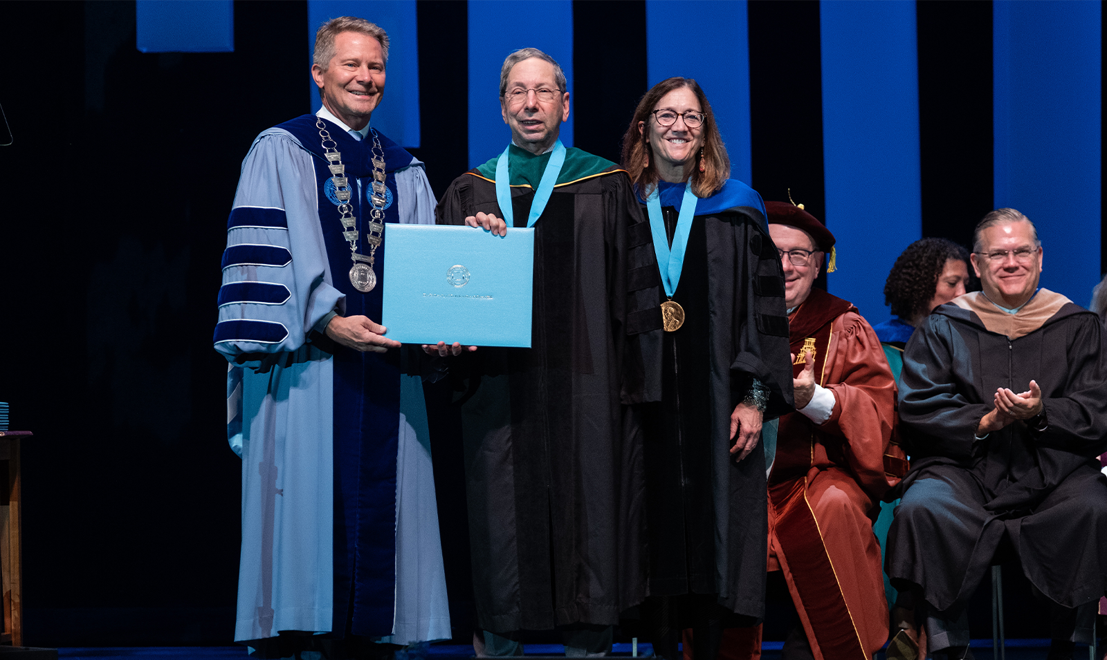 An award winner posing for photos on a stage with University leaders.