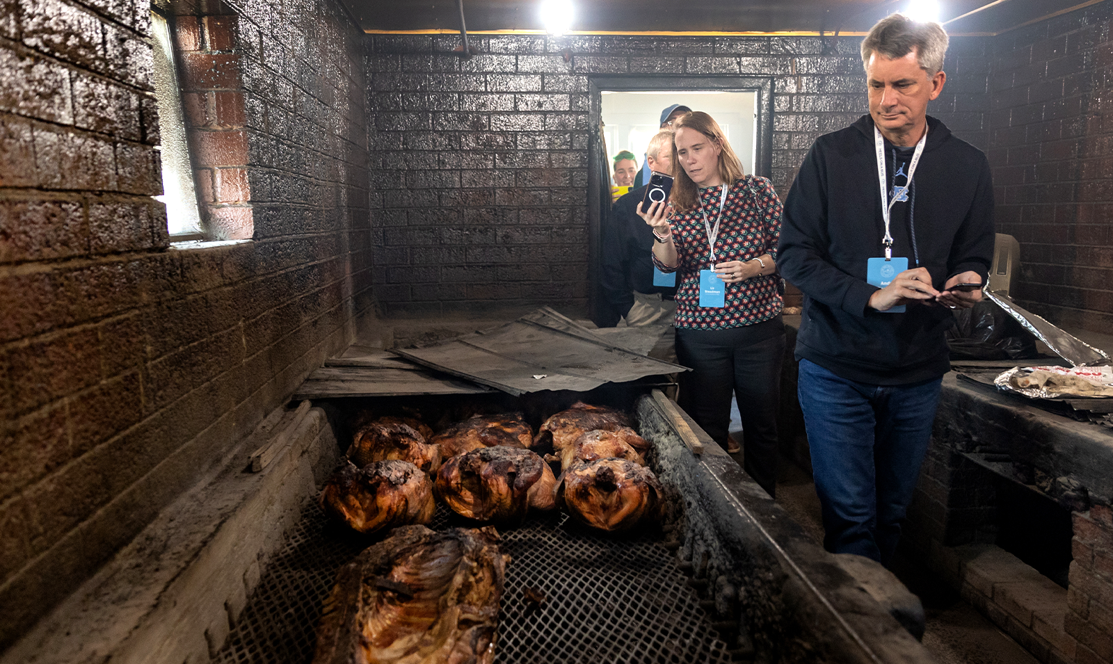 Tar Heel Bus Tour participants walk by hardwood coals in a barbecue reasaurant.