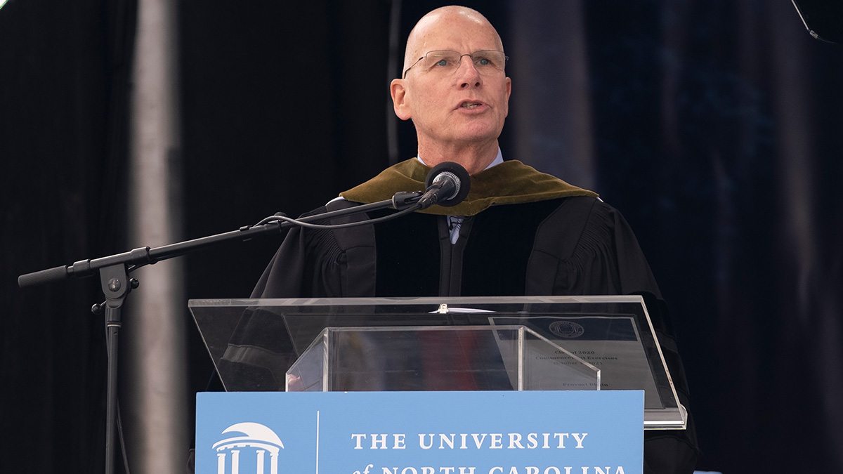 Bob Blouin wearing commencement robes speaking at a podium that reads 