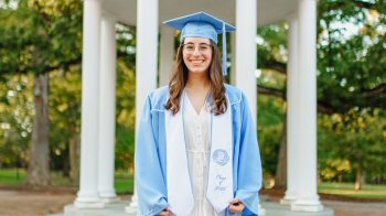 Emma Cohn poses in front of Old Well with Carolina Blue graduation robes.