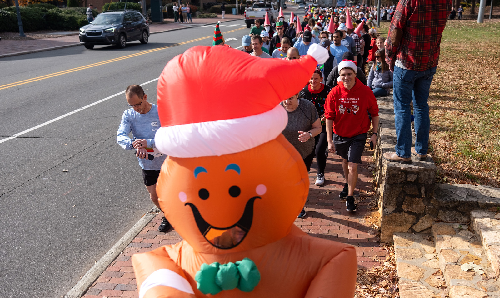 A person dressed up in a Gingerbread Man costume leading a group of joggers.