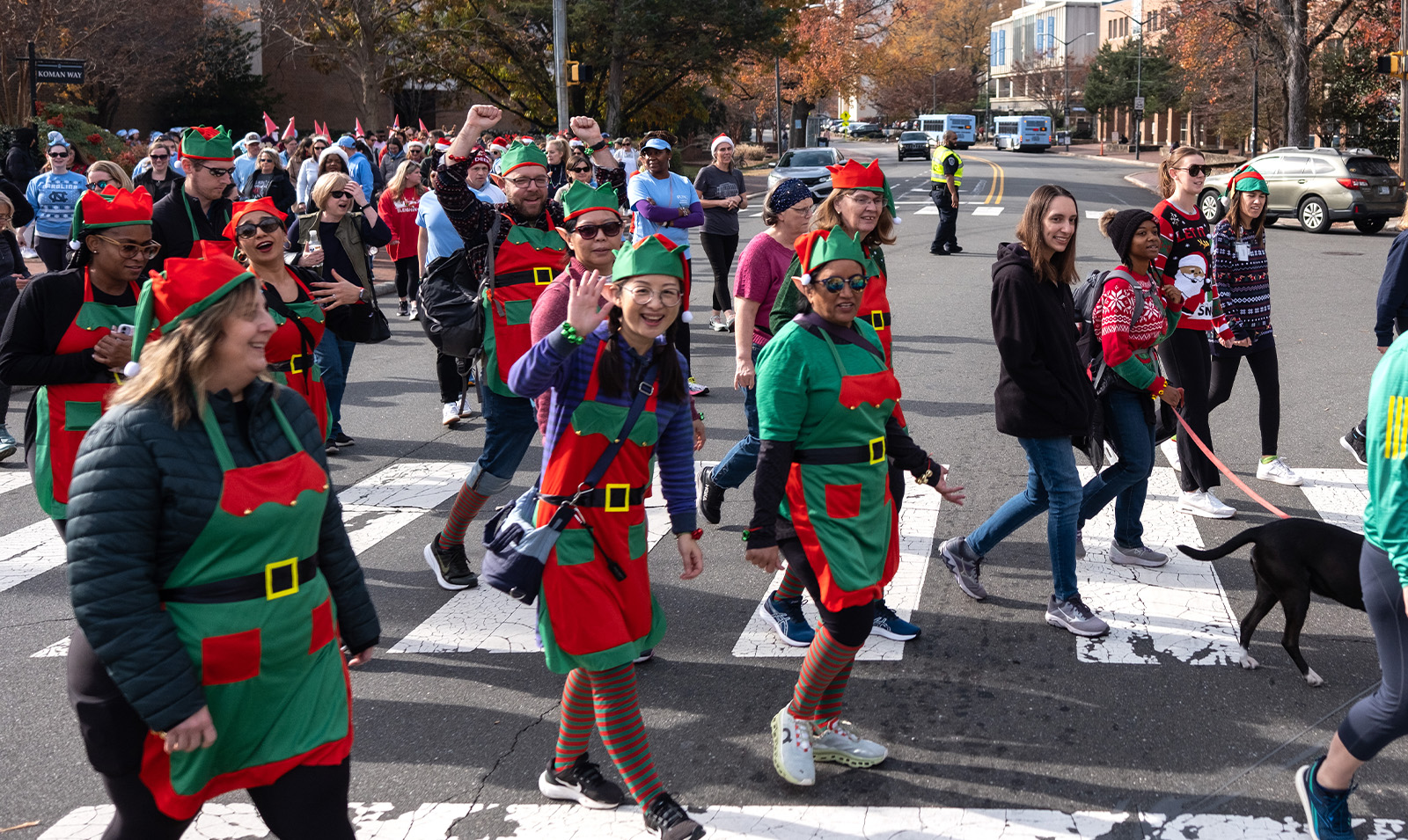 A group of walkers, some dressed up as elves, waving as they cross the street.