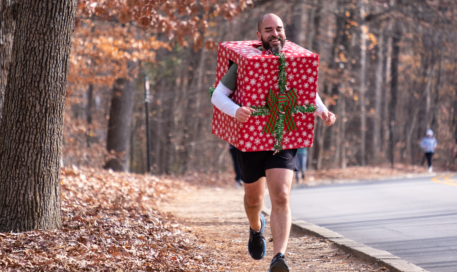 A man in a Christmas gift box costume jogging.