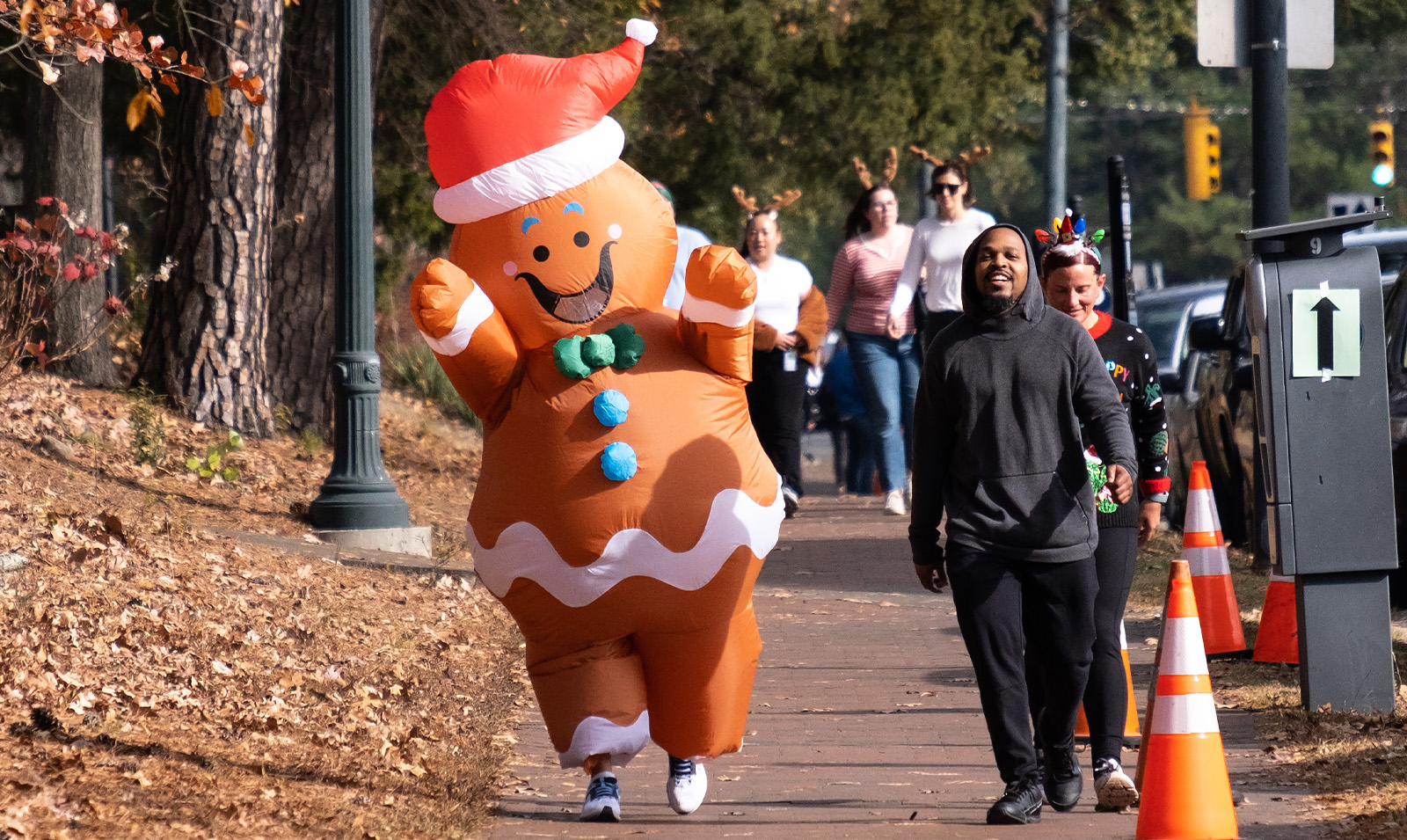 A man smiling as a jogger dressed up as a Gingerbread Man passes by him.