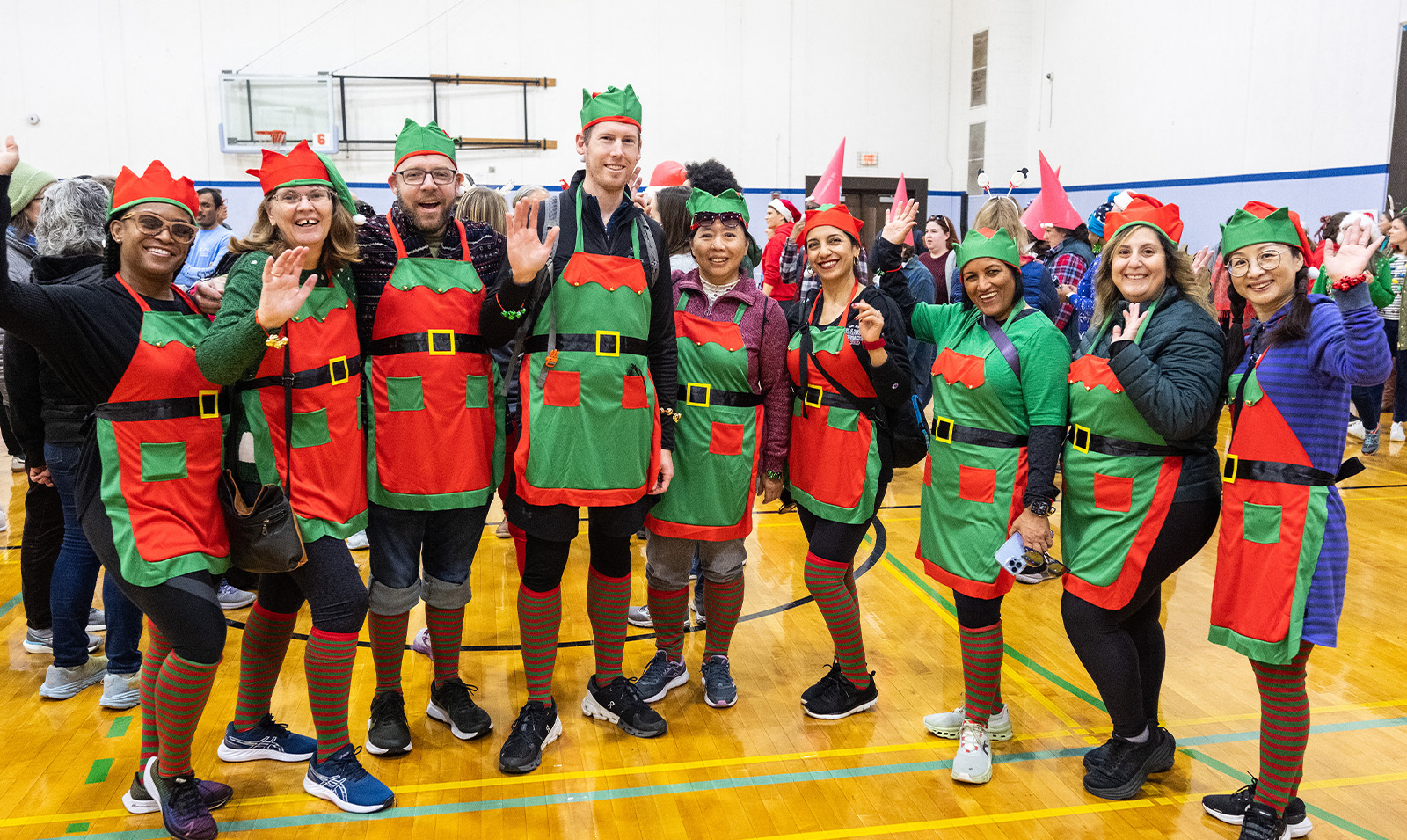 A group of employees dressed up as elves posing for a group photo in a gym.