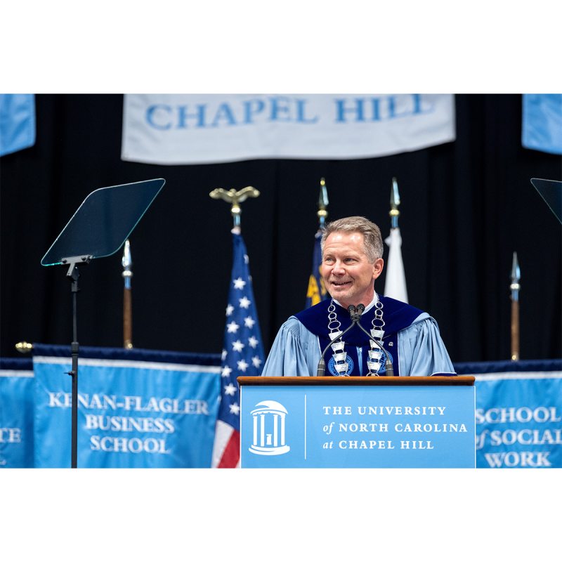 Chancellor Kevin M. Guskiewicz in regalia and giving a speech at a dais at Winter Commencement.