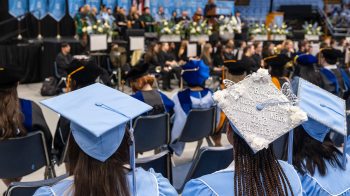 Photo from behind of a graduate at Winter Commencement whose self-designed cap reads: 