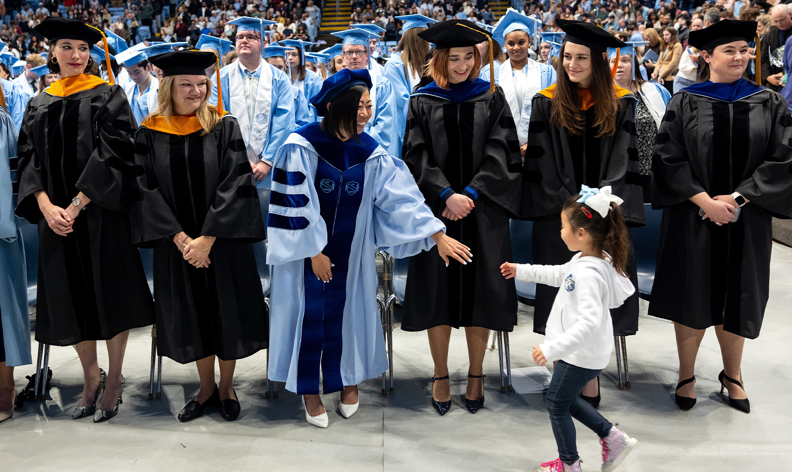 A young girl giving a faculty member a fist bump at Winter Commencement.