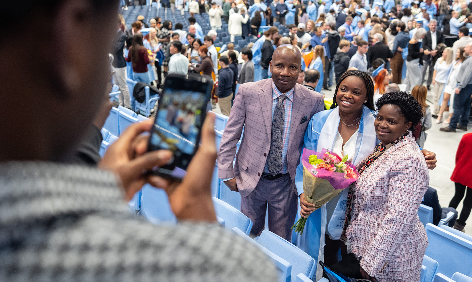 Photo of a person using their iPhone to take a picture of a graduate and two family members.