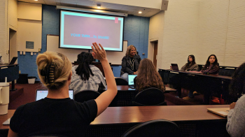 Professor Dixon-Green sits amongst students in classroom, some of which are raising hands in the foreground.