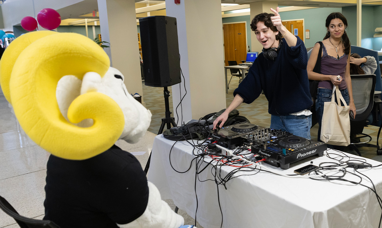 A ram mascot, Rameses, sitting attentively as a DJ plays music.