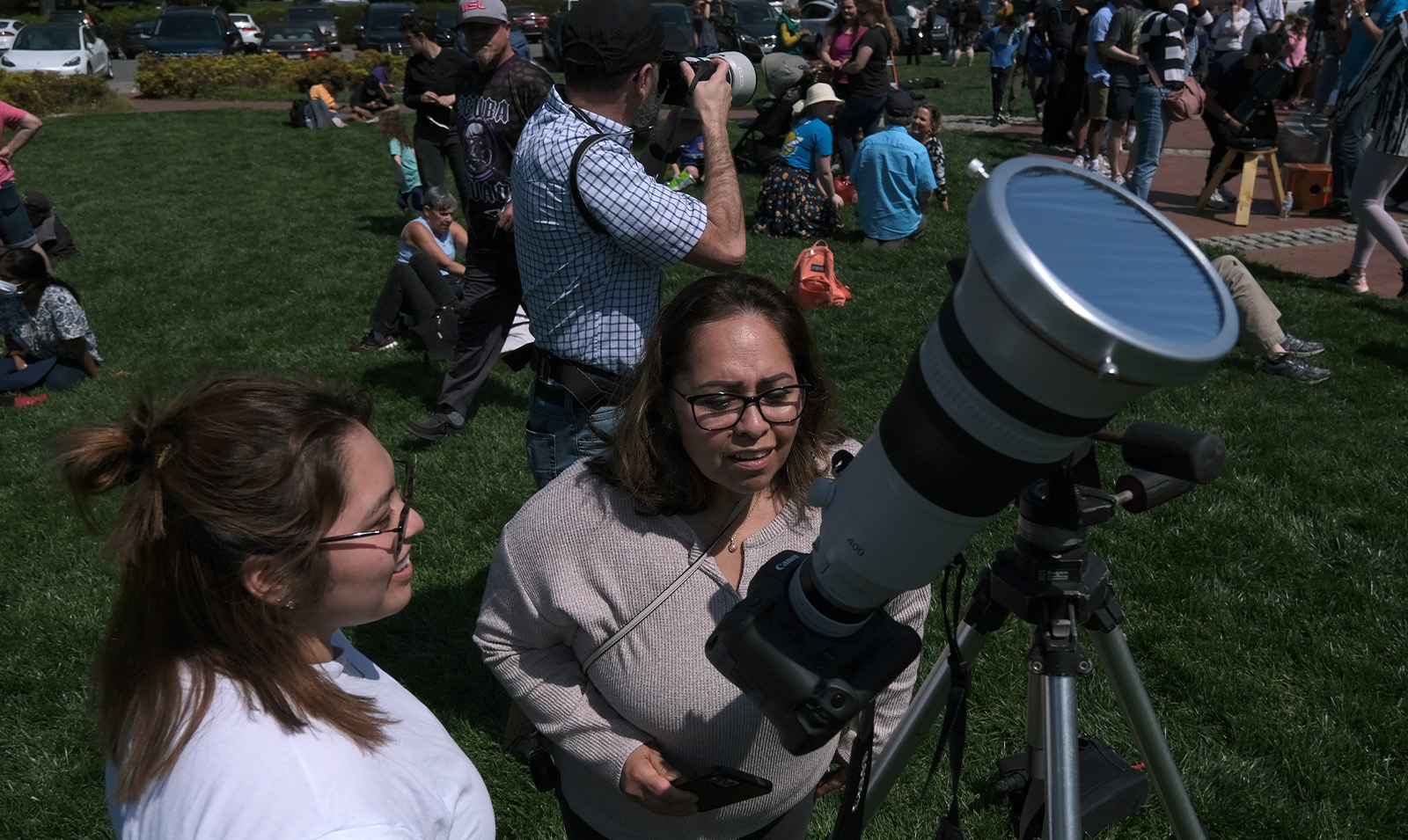 Two women standing by a telescope at a solar eclipse viewing party.