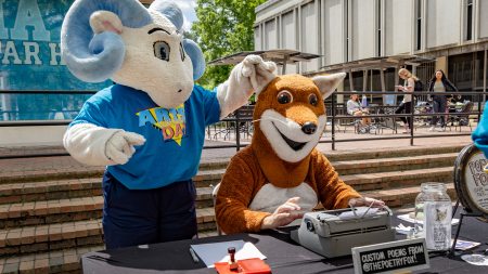 A ram mascot, Rameses Jr., holding the ear of another mascot, Poetry Fox, at Arts Everywhere Day.