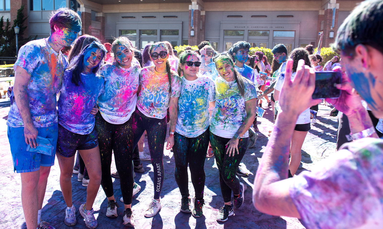 Crowd of students covered in paint celebrating Holi and posing for a group photo.