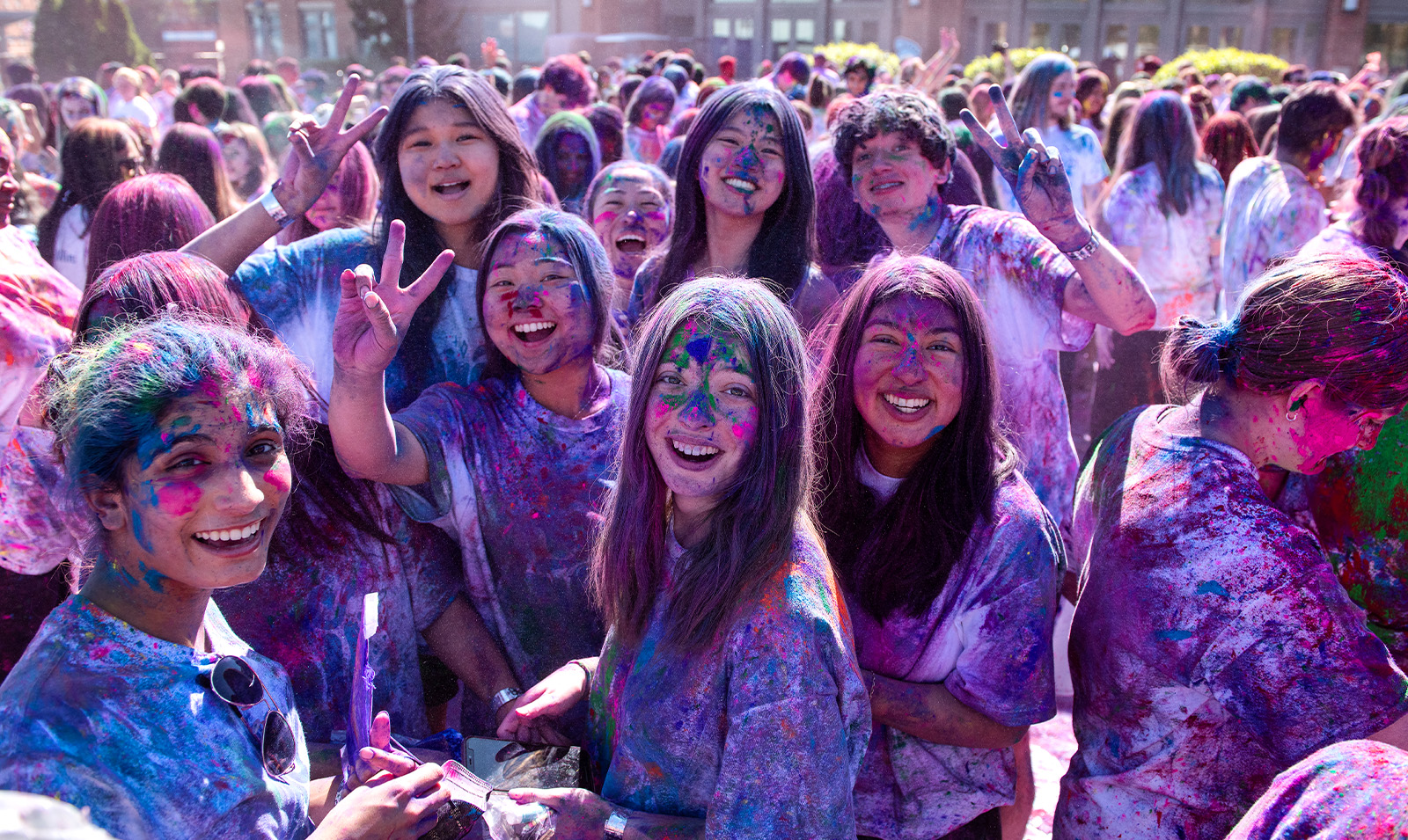 Group of students on a field celebrating Holi and covered in paint