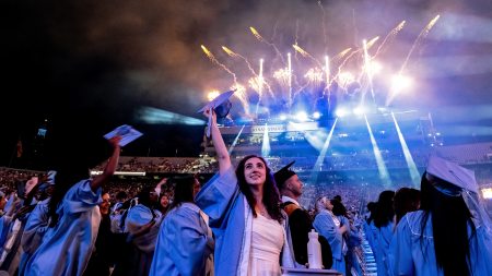 Student holds cap in air as fireworks go off