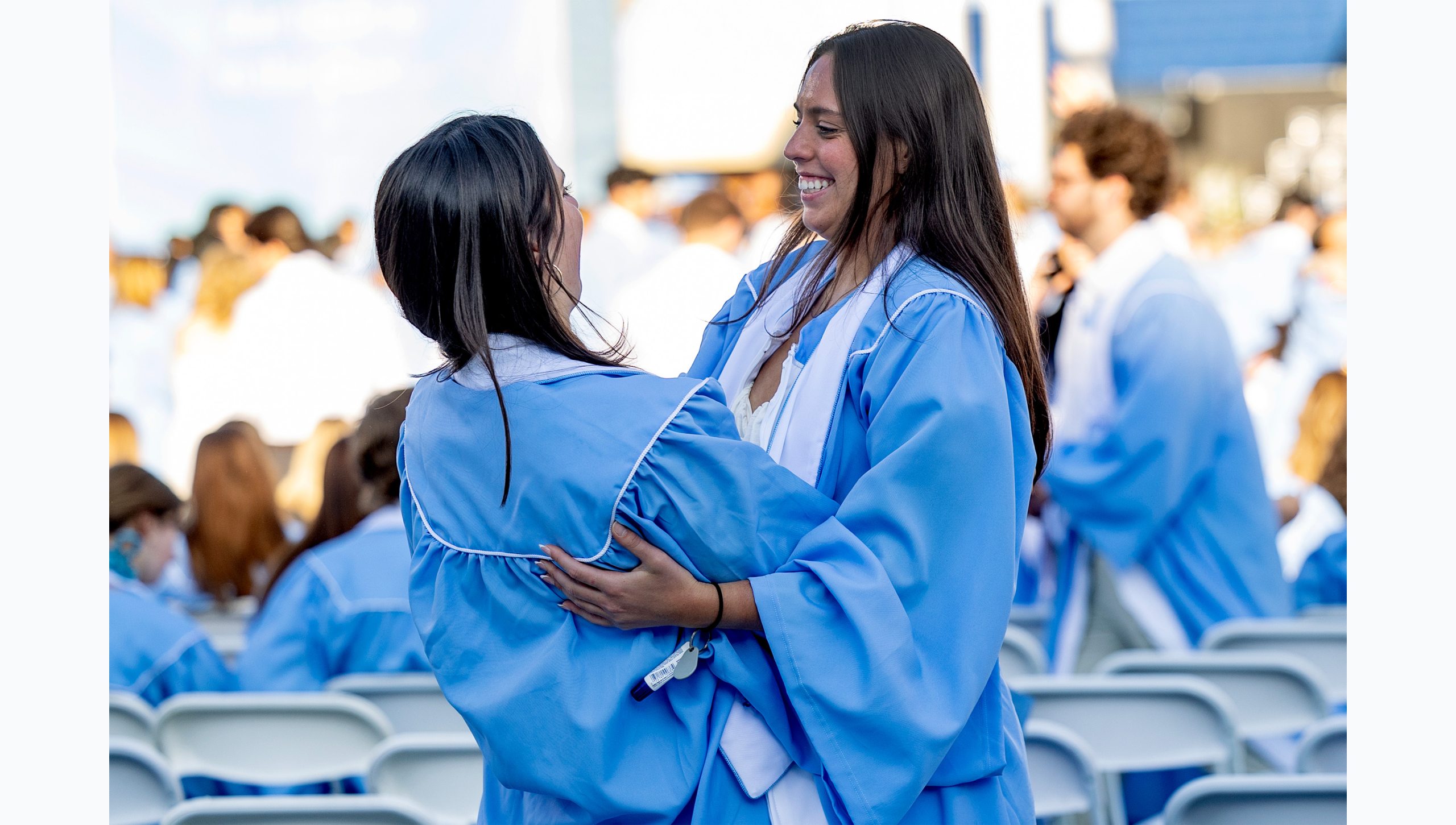 Graduates hug on field before ceremony