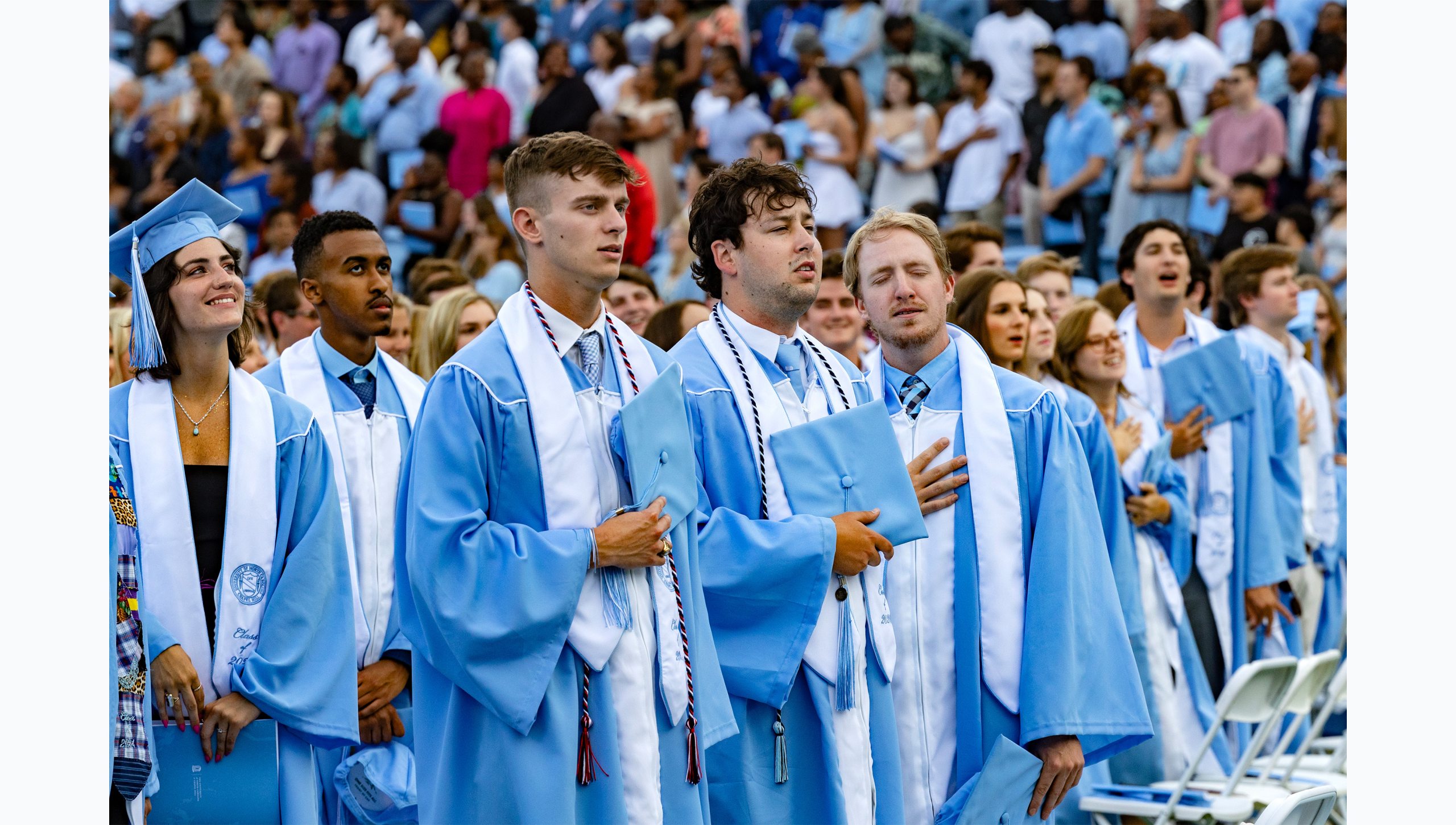 Graduates hold caps over hearts during national anthem