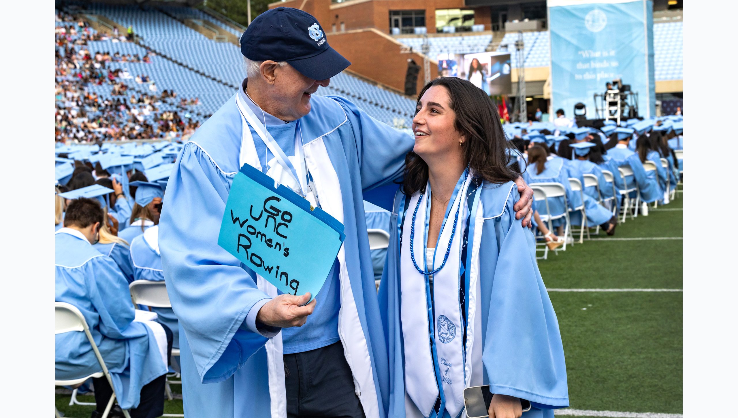 Graduate and adult smile at each other on field before ceremony