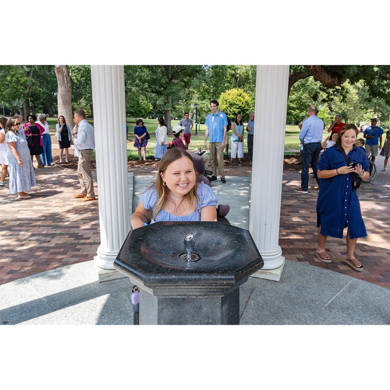 A student using a wheelchair approaching the fountain of the Old Well on the campus of UNC-Chapel Hill.