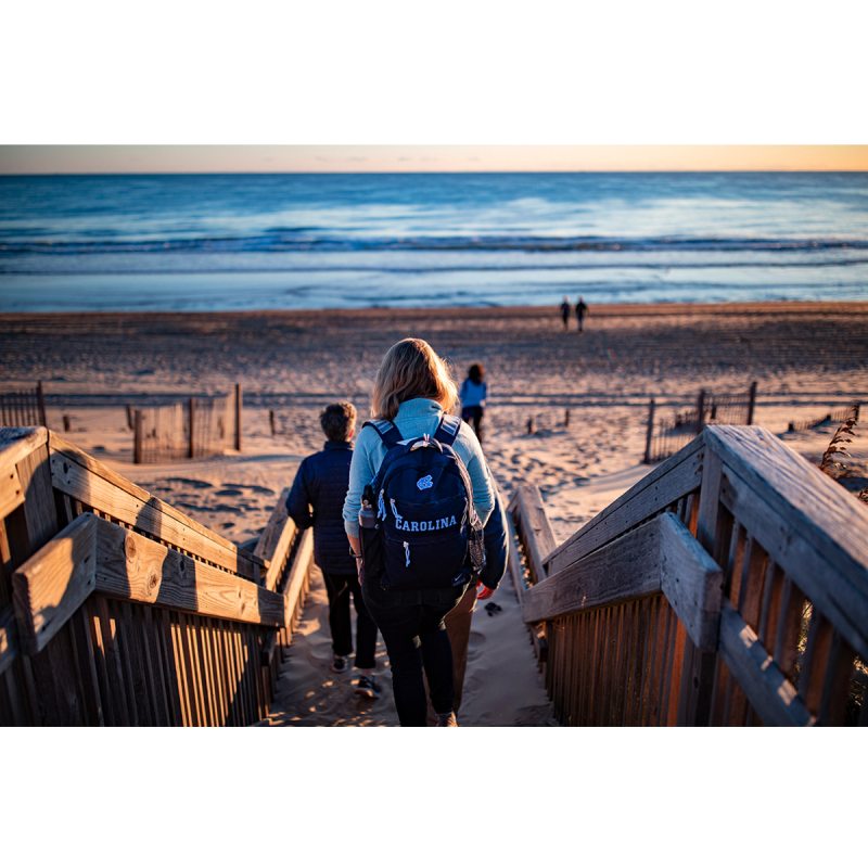 Woman with Carolina backpack walks toward the ocean at the beach