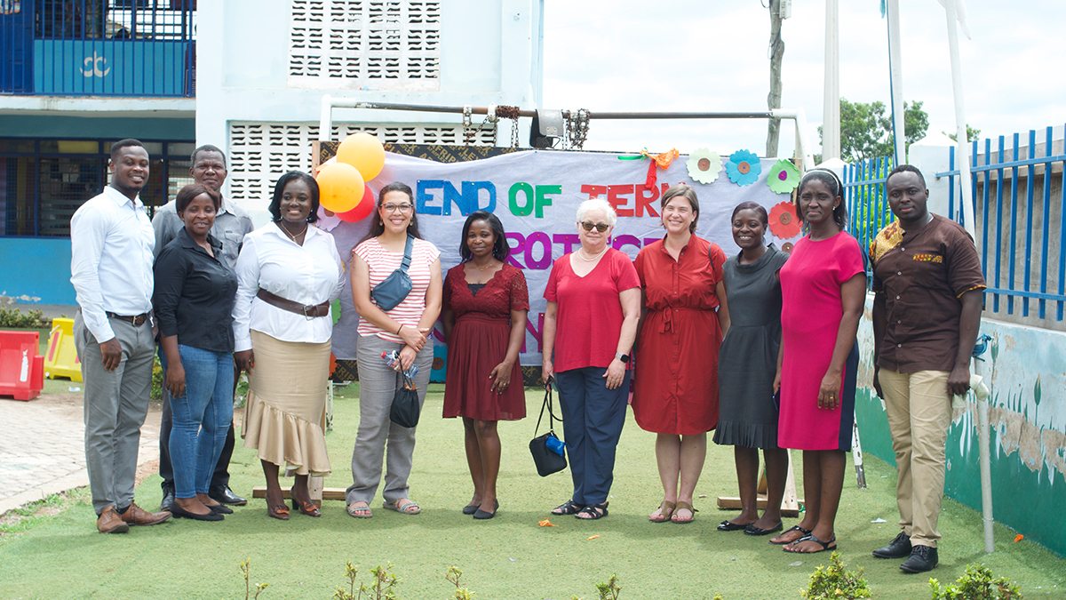 Teachers from North Carolina stand in front of a sign in Ghana celebrating the end of the school year.