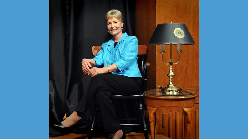 Brenda Kirby seated next to table with a lamp on her left.