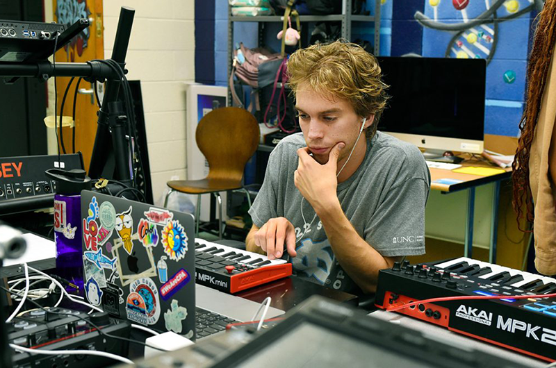 A male student wearing earbuds sits in front of a keyboard.