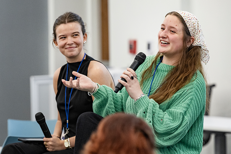 Two women speaking to an audience of high school students. One is holding a microphone.
