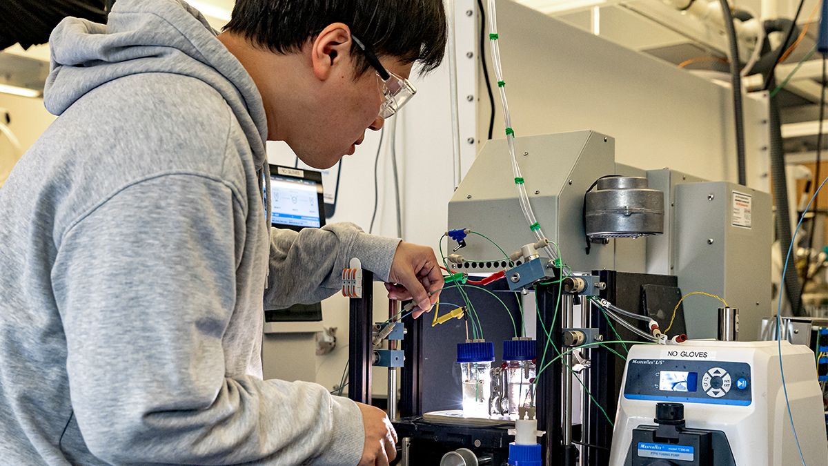 Hueynwoo Yang wearing sweatshirt and filling liquid vials with machinery at the Chase Solar Hub lab.