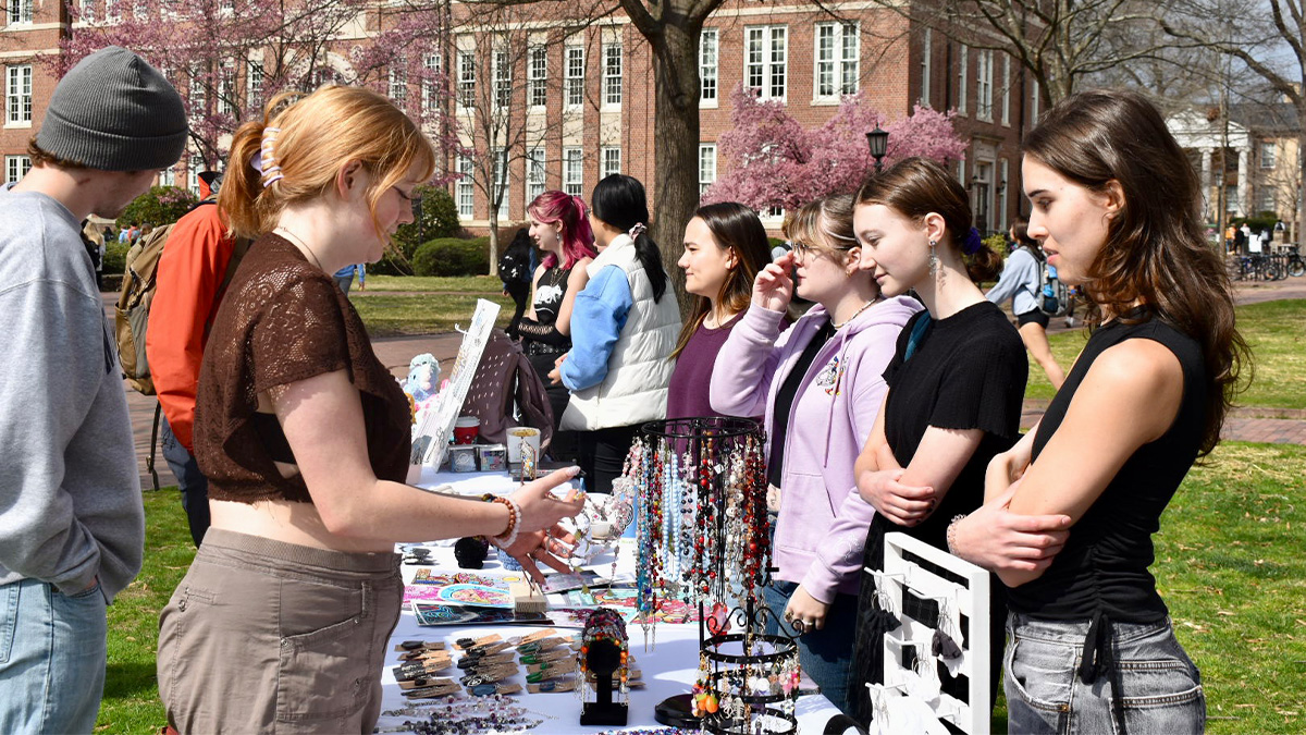 A group of students looking at jewelry and other crafts at a table at a pop-up event on Polk Place on the campus of UNC-Chapel Hill.