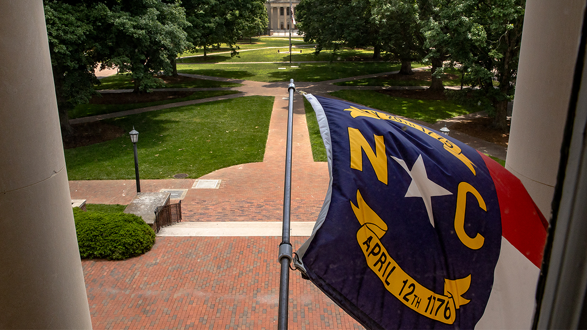 Photograph of the North Carolina flag hanging from South Building.
