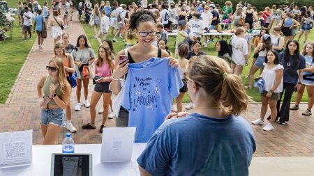 A student holding up a Carolina Blue T-shirt that reads 