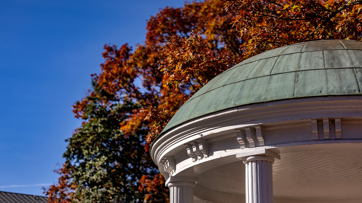 Dome and pillars of the Old Well with fall-time orange and red leaves seen in the background.