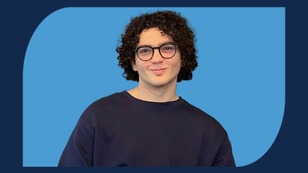 Ahmet sitting down in hallway with Carolina Blue borders surrounding the image.