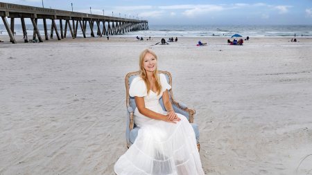 Isabella Cox sitting in a Carolina Blue chair on a beach with the Atlantic Ocean and a pier seen in the background.