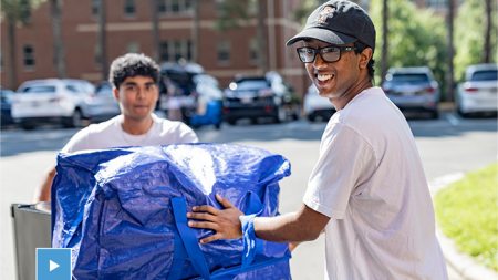 Two students using a dolly to move into a dorm.