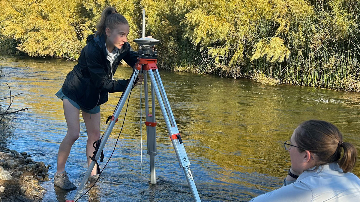 Student sets up tripod on river bank.