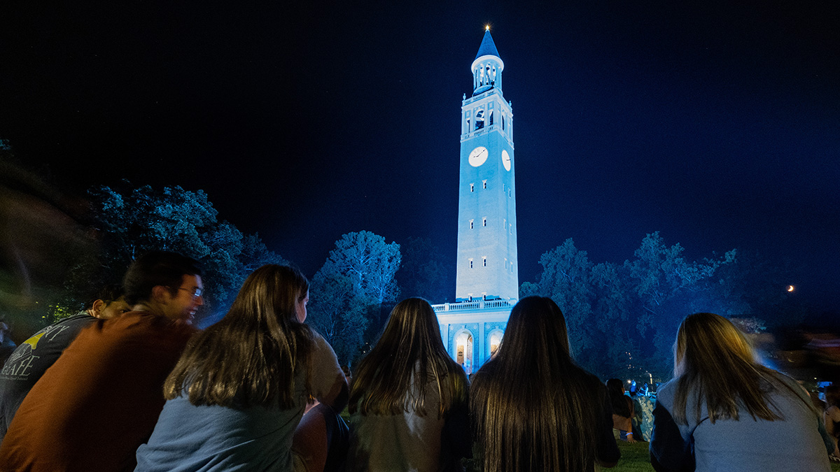 Students watching the lighting of the Bell Tower Carolina Blue at night the day before the first day of classes.