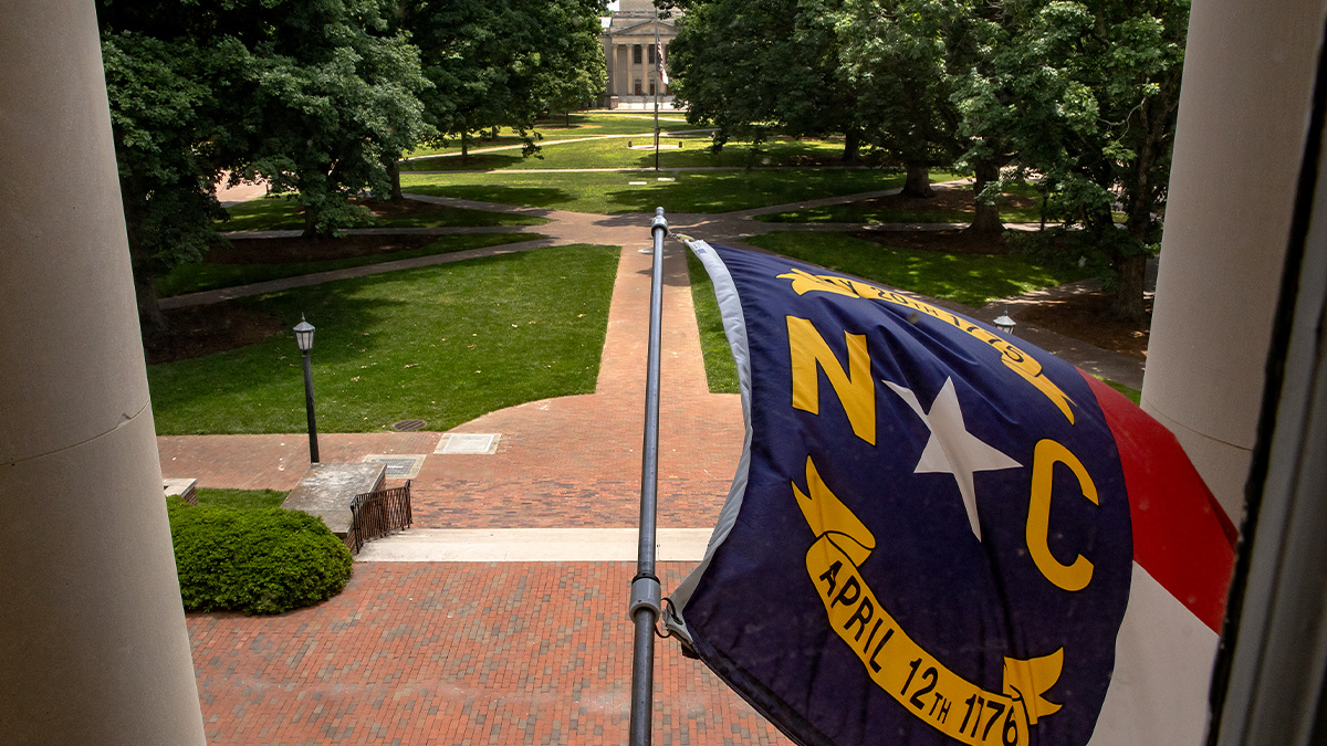 North Carolina state flag flying from South Building with view of Polk Place in the background on the campus of UNC-Chapel Hill.