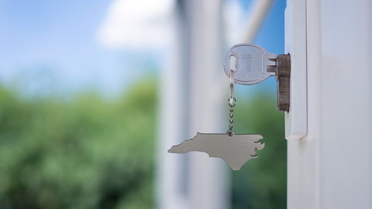 A key in a door with a keychain in the shape of North Carolina.