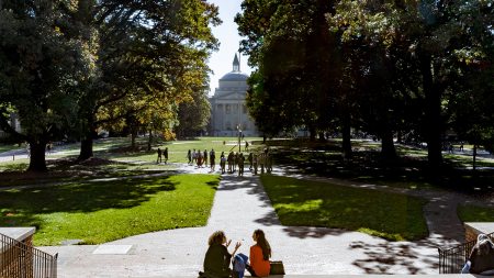 Main UNC quad during the day with students sitting on steps of South Building in foreground.