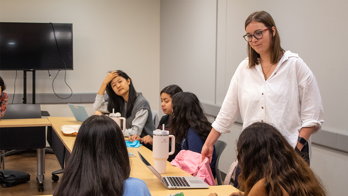 Woman wearing white top standing in front of students in conference room.