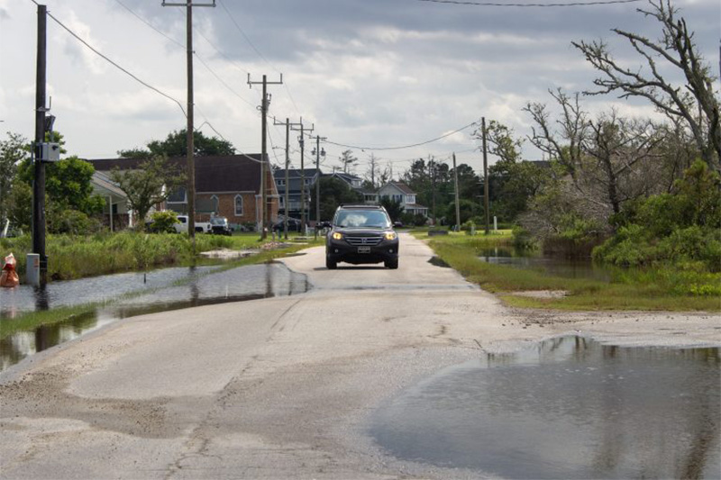 Car driving down a partially flooded street.