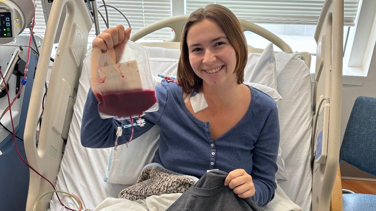 Samantha Lewis holding container of her own blood in hospital bed.