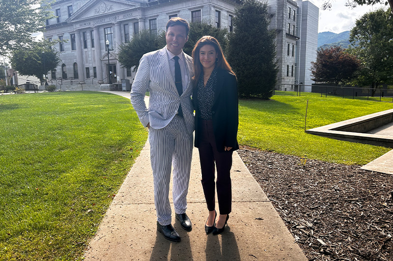 Tazanna Jones and Zeb Smathers posing for a photo on a sidewalk outside of a governmental building.