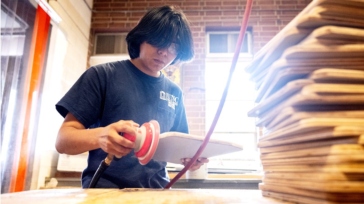 Alex Escobedo wearing safety goggles and sanding objects in the UNC carpentry shop.